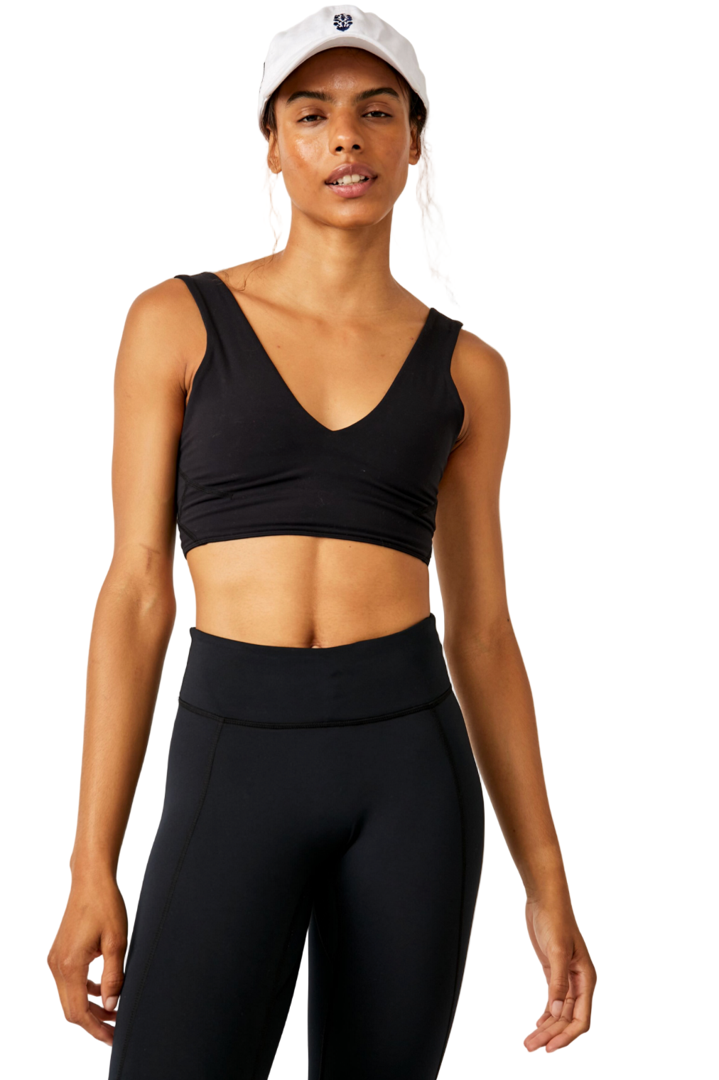 Woman wearing a black sports bra and leggings with a white cap on a light background