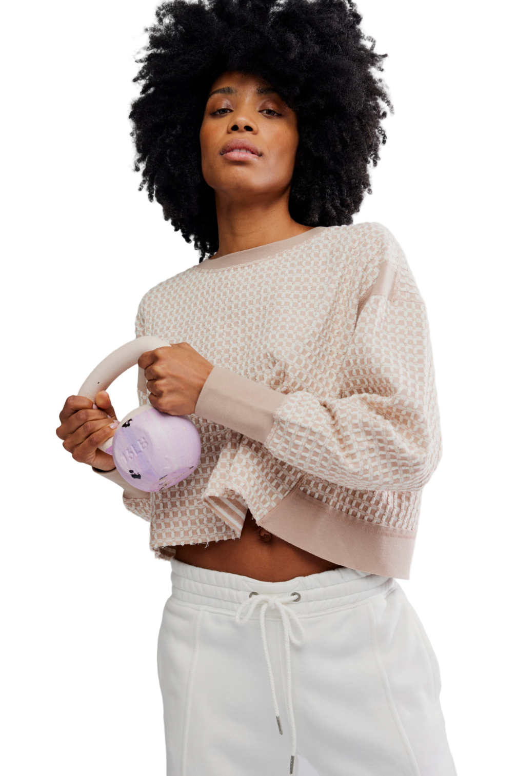 Woman wearing a beige sweater and white pants holding a pink plush toy against a plain background