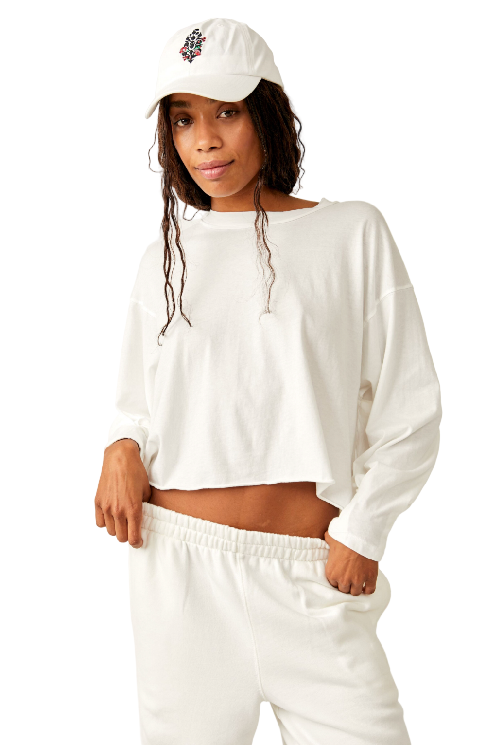 Woman wearing a white long-sleeve crop top and pants with a white cap on a white background