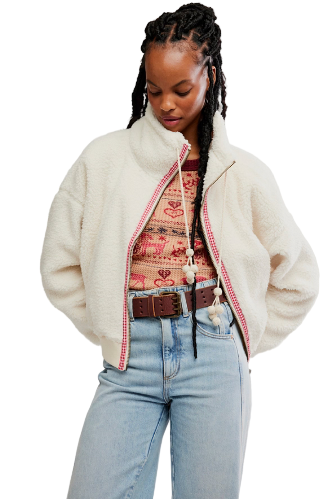 Person wearing a cream jacket over a patterned top with light blue jeans on a plain background