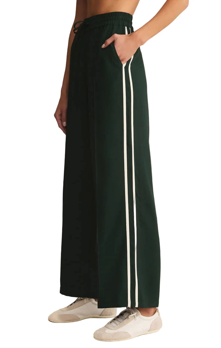 Green wide-leg pants with white stripes worn by a person on a beige background