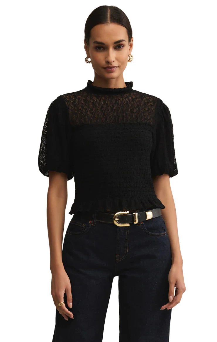 Woman wearing a black lace top and dark jeans against a beige background