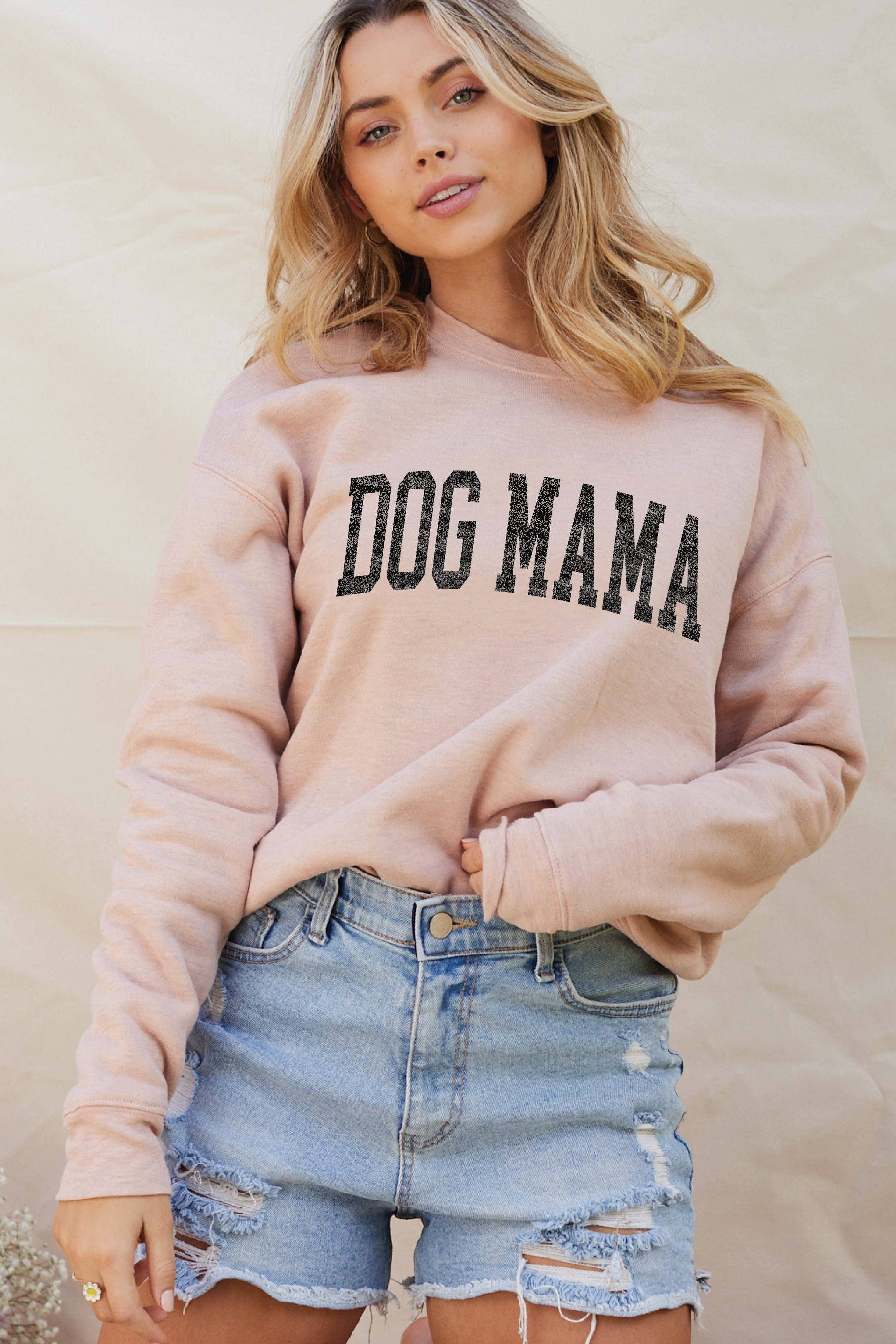 Woman wearing a pink 'DOG MAMA' sweatshirt and denim shorts against a neutral background