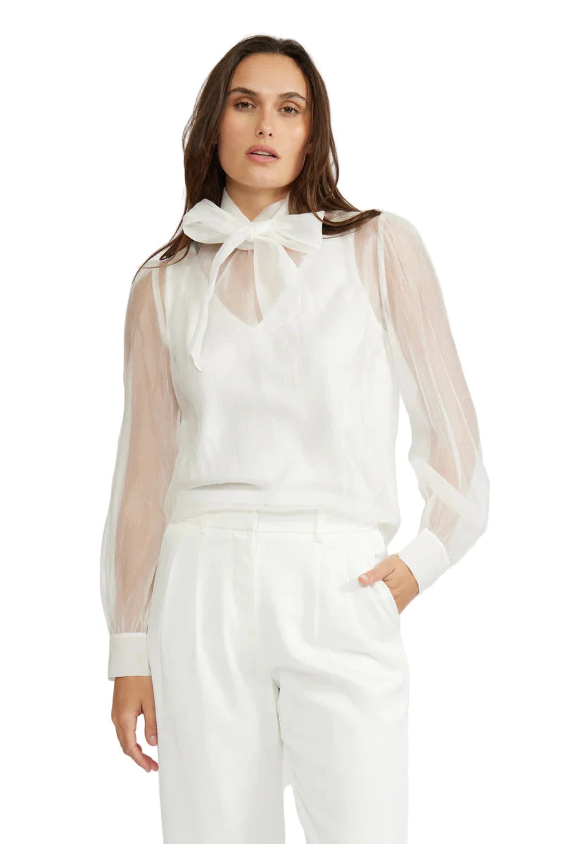 Woman wearing a white outfit with sheer sleeves against a white background