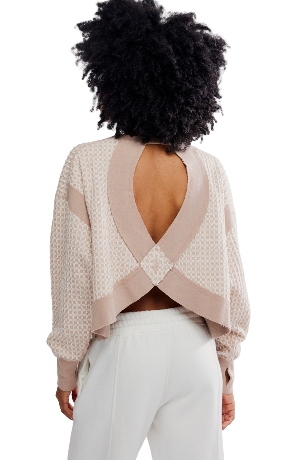 Person wearing a beige open-back top and white pants on a plain background