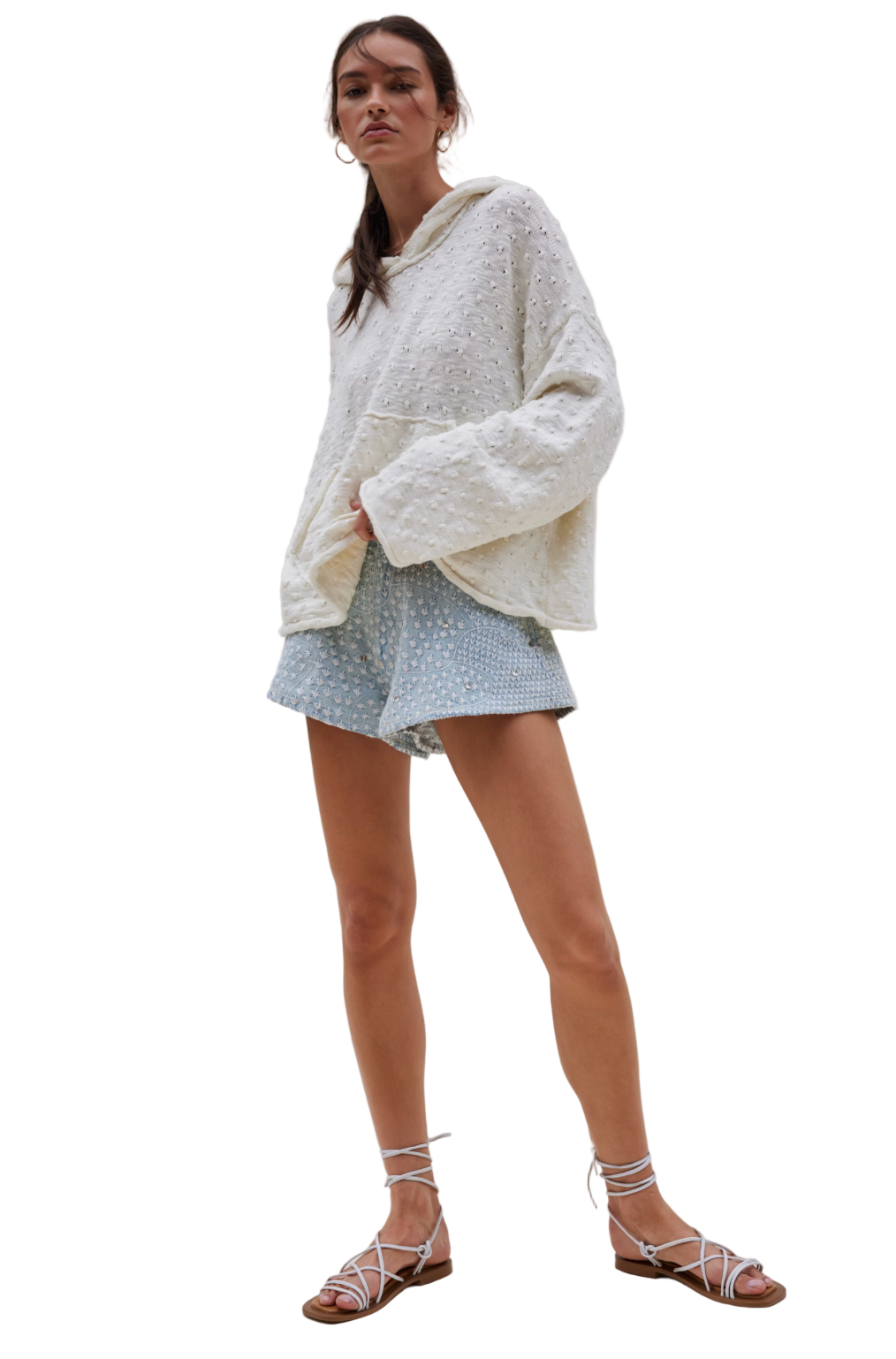 Woman wearing a white oversized sweater and light blue polka dot shorts on a plain background