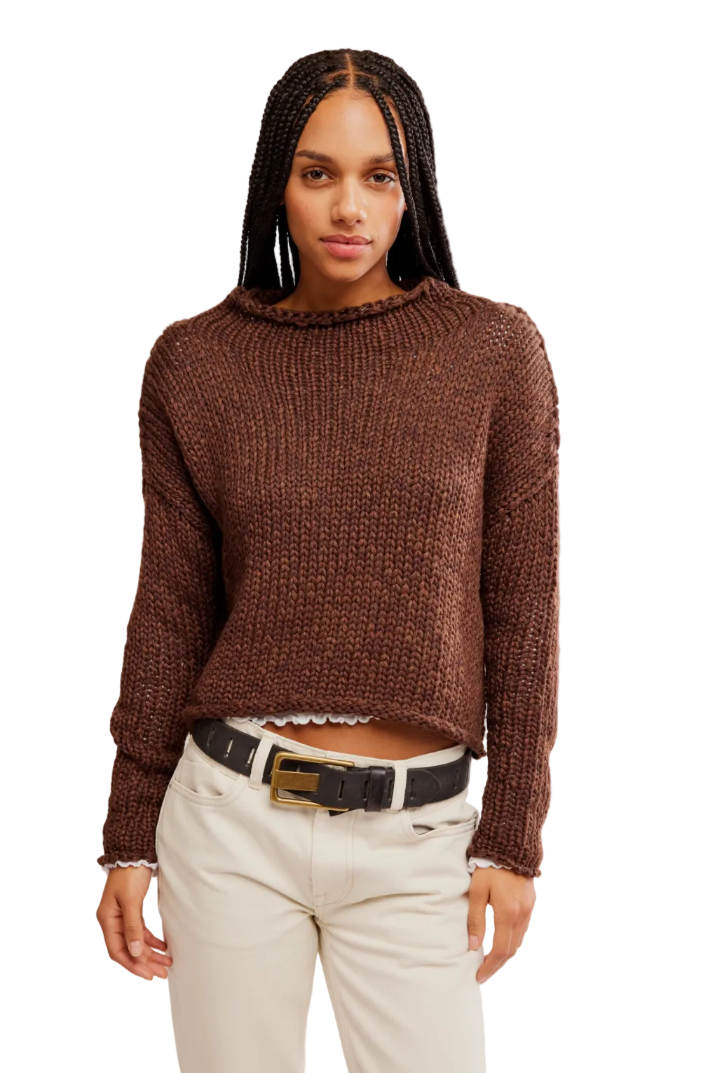 Woman wearing a brown sweater and white pants against a plain background
