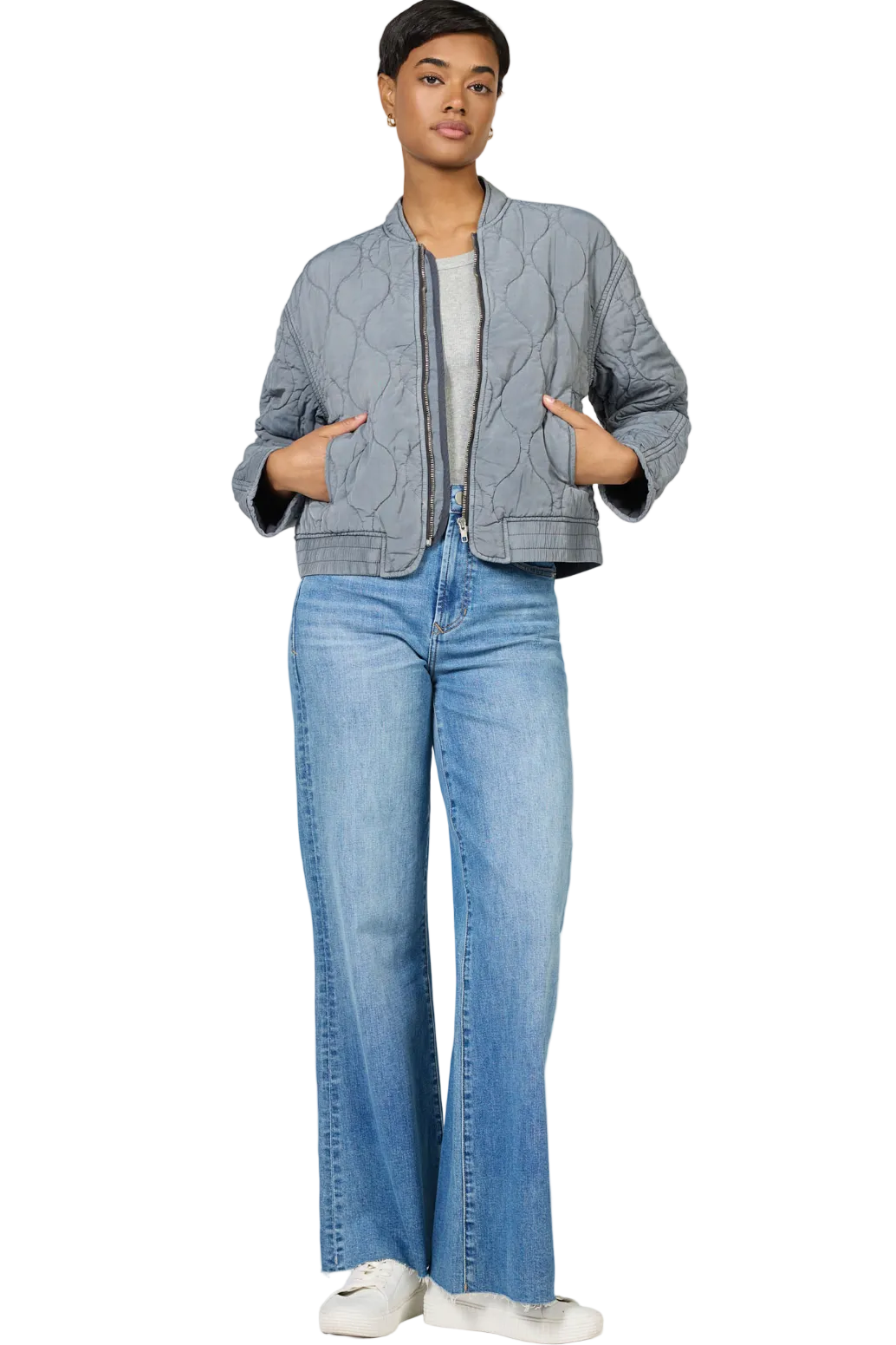 Person wearing a gray quilted jacket and blue jeans on a white background