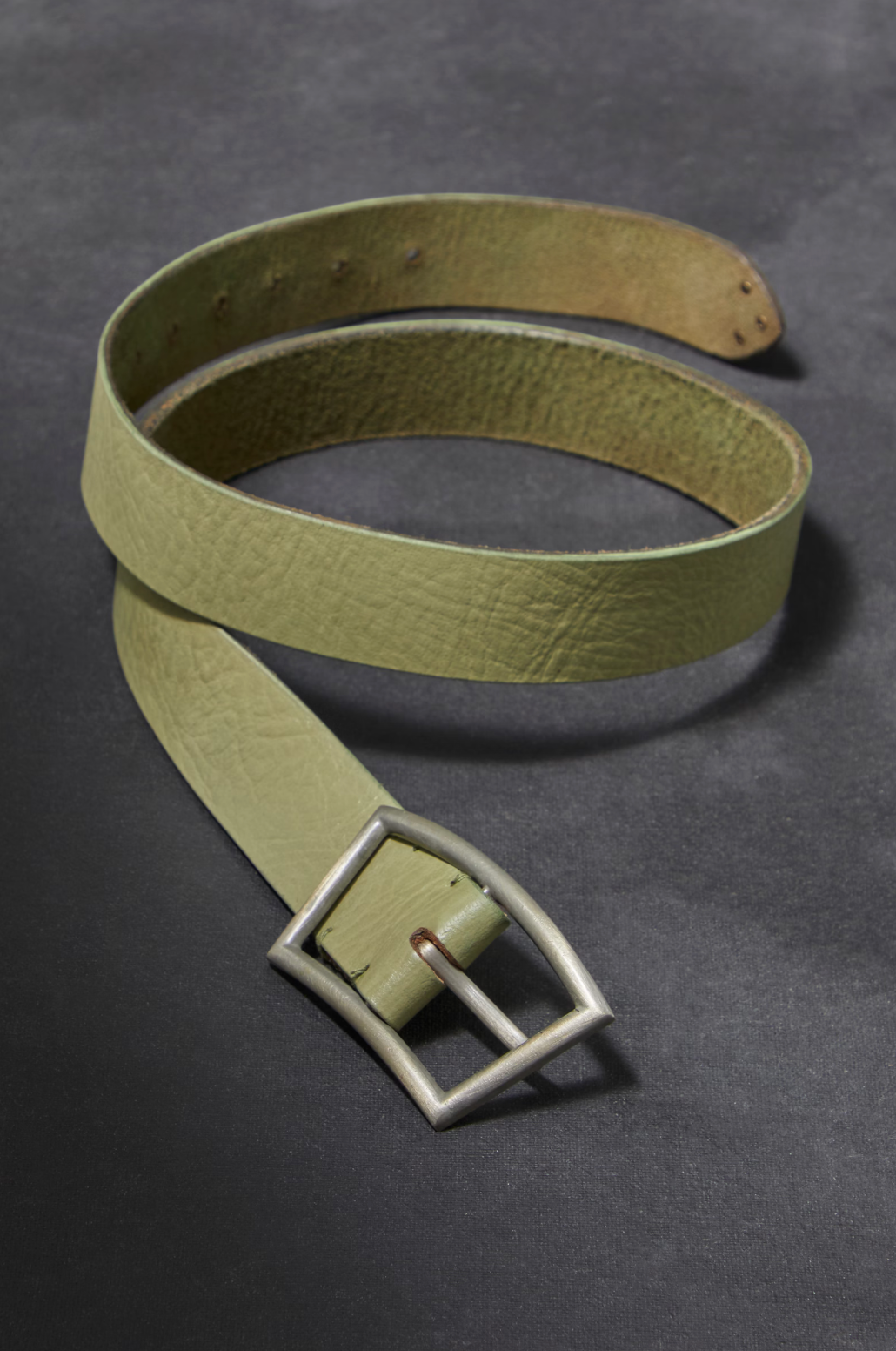 Green leather belt with a silver buckle on a gray background