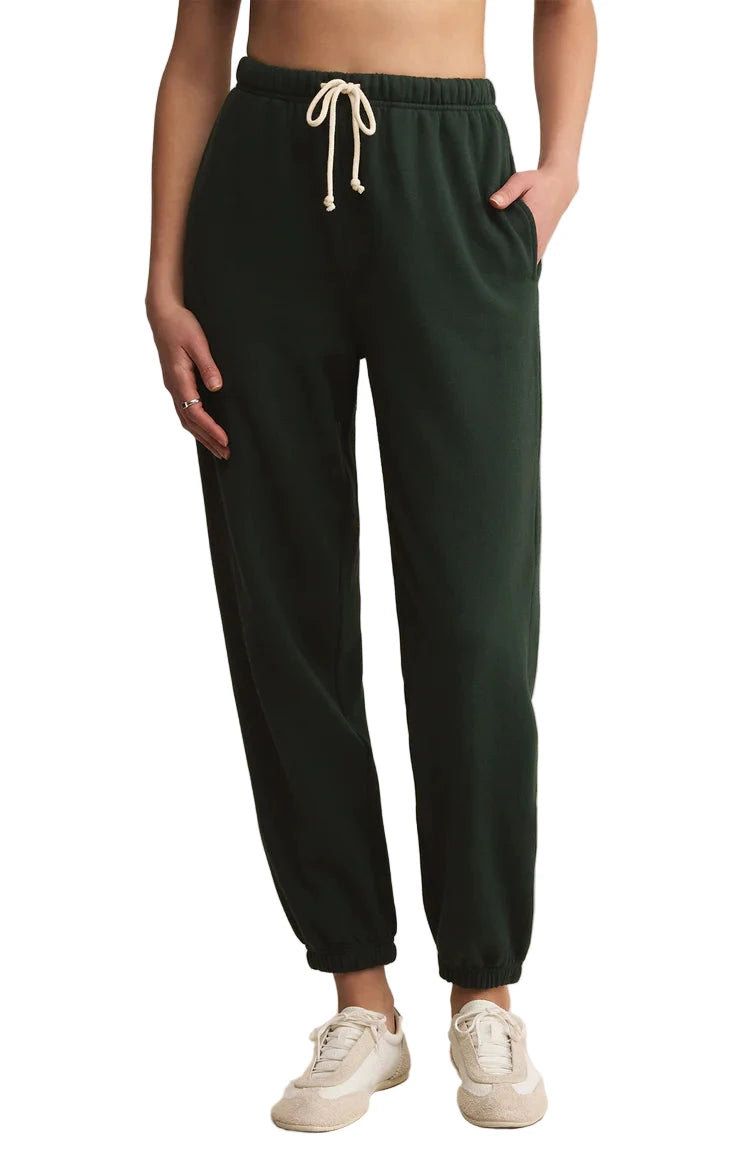 Dark green sweatpants with a white drawstring worn by a person on a beige background
