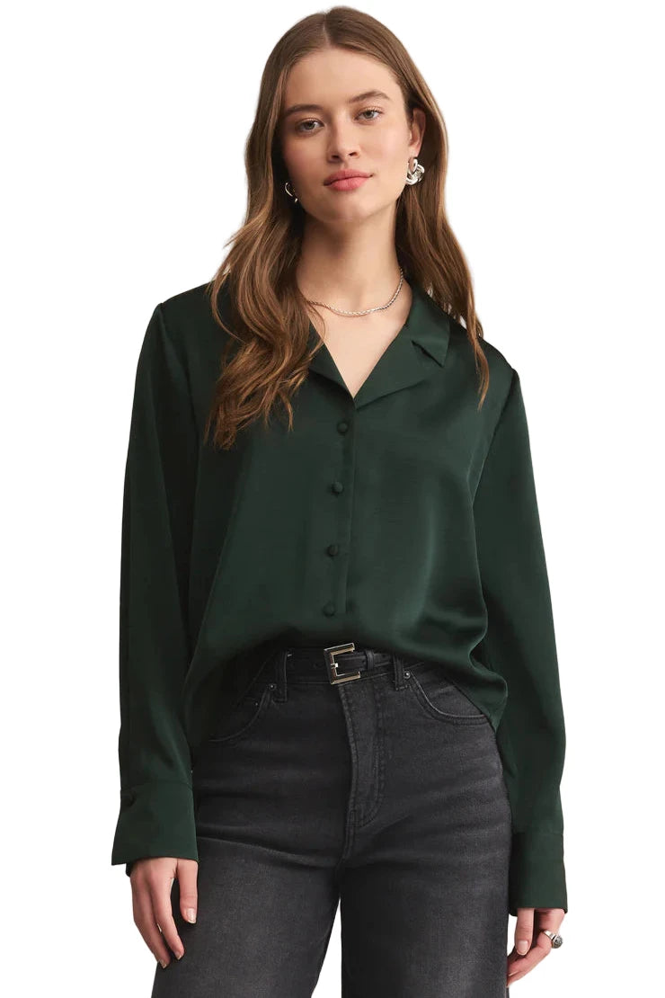 Woman wearing a green blouse and black pants against a beige background